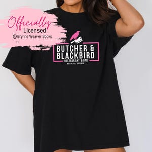 以下が含まれることがあります： 黒のTシャツに、ピンクのロゴがプリントされています。ロゴには「Butcher & Blackbird Restaurant & Bar Boston, MA Est. 2023」と書いてあり、ピンクのシルエットで描かれたナイフを持った鳥もデザインされています。