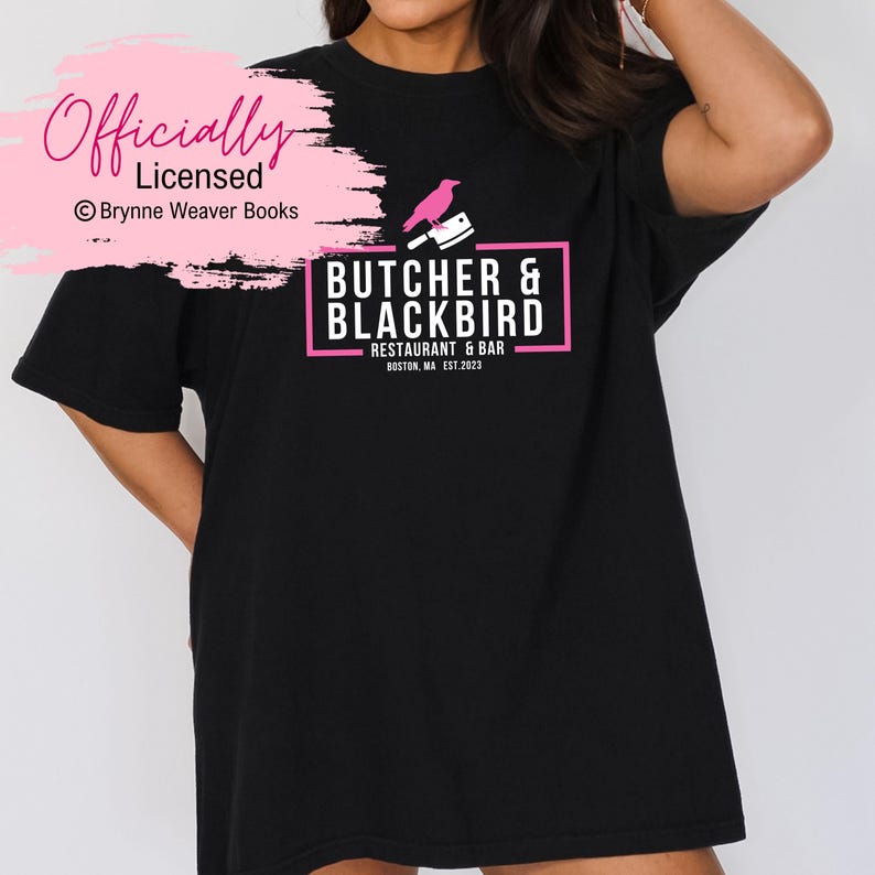 以下が含まれることがあります： 黒のTシャツに、ピンクのロゴがプリントされています。ロゴには「Butcher & Blackbird Restaurant & Bar Boston, MA Est. 2023」と書いてあり、ピンクのシルエットで描かれたナイフを持った鳥もデザインされています。