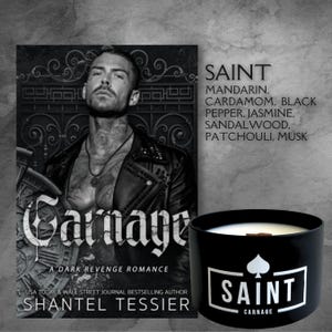 May include: A black candle with a white label that says "SAINT CARNAGE". The candle is in front of a book cover with a man on it. The book cover says "Carnage A Dark Revenge Romance" and "Shantel Tessier".