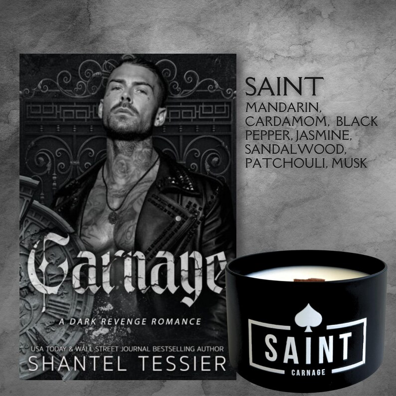 May include: A black candle with a white label that says "SAINT CARNAGE". The candle is in front of a book cover with a man on it. The book cover says "Carnage A Dark Revenge Romance" and "Shantel Tessier".