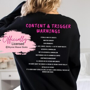 May include: Black sweatshirt with pink text that reads "Content & Trigger Warnings" and "Officially Licensed Brynner Weaver Books". The text lists various content warnings, including "eyeballs and eye sockets", "amateur surgery", "skin ornaments", "ws, axes, knives, scalpels - a lot of sharp objects", "accidental cannibalism", "not-so-accidental cannibalism", "questionable use of a mummified corpse", "lobotomized manservant", "ill-advised use of kitchen implements", "I'm sorry about the cookies & cream ice cream (I'm not really)", "detailed sex scenes", "it's a book about serial killers, so there's some generally messed-up murder and chaos".