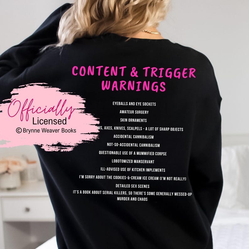 May include: Black sweatshirt with pink text that reads "Content & Trigger Warnings" and "Officially Licensed Brynner Weaver Books". The text lists various content warnings, including "eyeballs and eye sockets", "amateur surgery", "skin ornaments", "ws, axes, knives, scalpels - a lot of sharp objects", "accidental cannibalism", "not-so-accidental cannibalism", "questionable use of a mummified corpse", "lobotomized manservant", "ill-advised use of kitchen implements", "I'm sorry about the cookies & cream ice cream (I'm not really)", "detailed sex scenes", "it's a book about serial killers, so there's some generally messed-up murder and chaos".