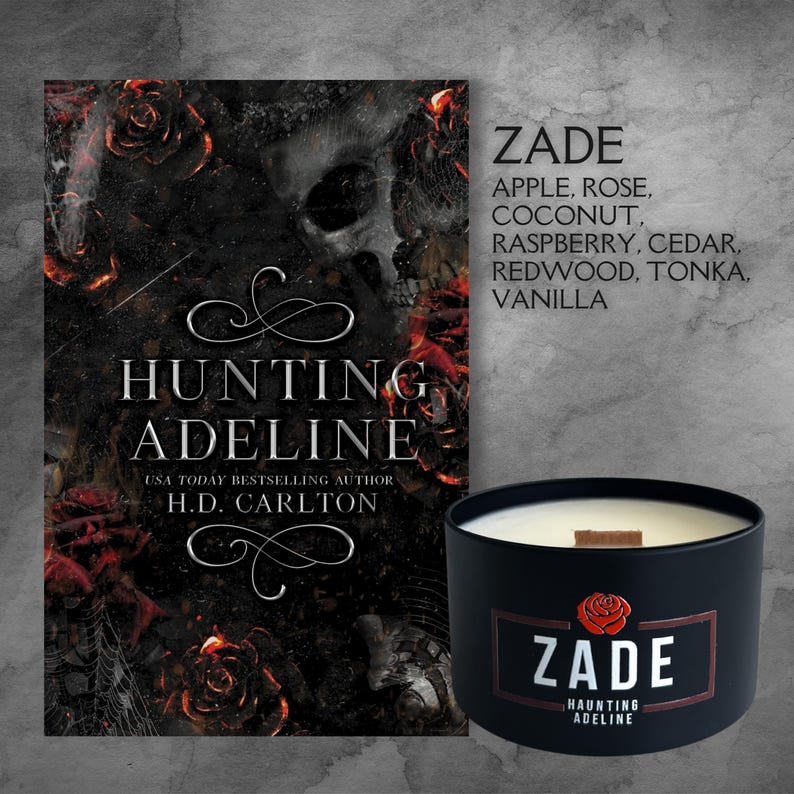 May include: A black candle with a white label that says "ZADE" and "HAUNTING ADELINE". The candle is next to a book cover with the title "HUNTING ADELINE" and the author's name "H.D. CARLTON". The book cover features a skull and roses.