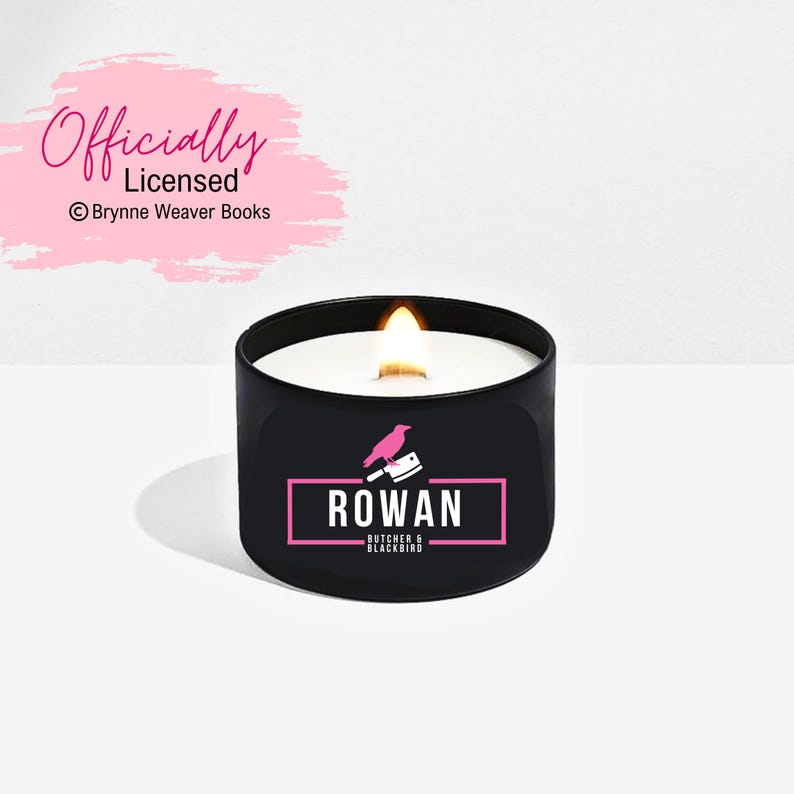 May include: A black candle with a pink logo that says "ROWAN Butcher & Blackbird" and a pink bird with a knife. The candle is lit and the flame is visible.