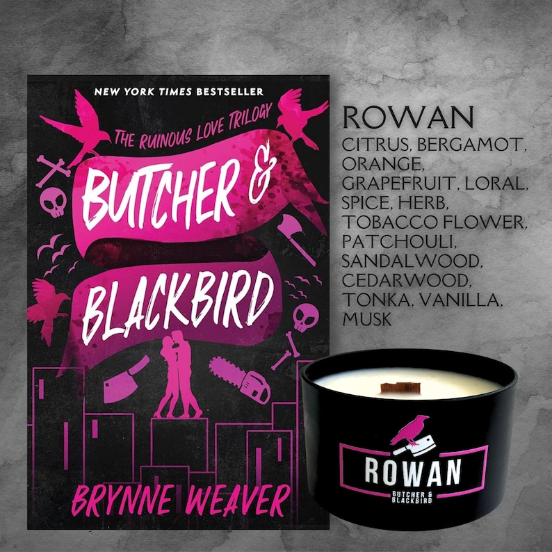 May include: A black candle with a wooden lid and a pink and black label that says "Rowan Butcher & Blackbird". The candle is sitting on a table in front of a book cover with the title "Butcher & Blackbird" and the author's name "Brynne Weaver".
