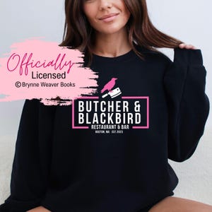 May include: Black sweatshirt with a pink graphic design that says "Butcher & Blackbird Restaurant & Bar Boston, MA Est. 2023" with a black crow holding a butcher knife.