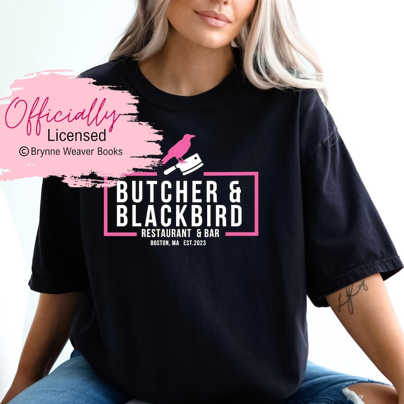以下が含まれることがあります： 「Butcher & Blackbird Restaurant & Bar Boston, MA Est. 2023」とピンク色のロゴが書かれた黒いTシャツ。ロゴには、ピンク色のナイフの上にピンク色の鳥がとまっているデザインも含まれています。