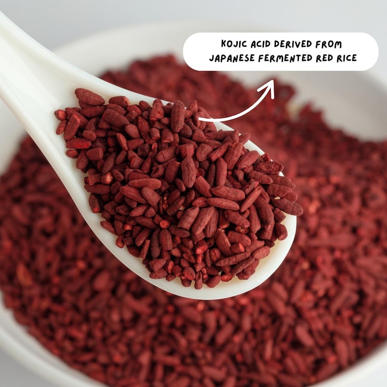 May include: A white spoon filled with red fermented rice. The text "KOJIC ACID DERIVED FROM JAPANESE FERMENTED RED RICE" is written above the spoon.