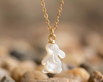 May include: A gold-toned chain necklace featuring a small, white, iridescent, carved mother-of-pearl pendant in the shape of a rabbit. The pendant hangs from a delicate metal link chain, showcasing a smooth, polished finish on the bunny figure.