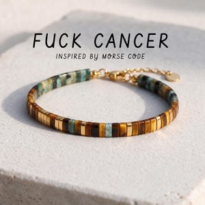 May include: A bracelet featuring brown tiger eye, teal, and gold-toned rectangular beads arranged in a pattern. The text FUCK CANCER INSPIRED BY MORSE CODE is displayed above the bracelet, which includes a gold-toned chain and clasp.