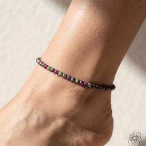 Peut inclure: Une chevillère composée de petites perles rondes et facettées, alternant des nuances de magenta profond et de vert forêt. Les perles sont enfilées selon un motif uniforme et continu, formant un bracelet circulaire délicat et coloré.