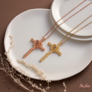 Puede incluir: Dos collares de cruz, uno en oro rosa y otro dorado, descansan sobre un plato blanco. Cada cruz presenta un centro en forma de coraz&oacute;n y est&aacute; adornada con peque&ntilde;as piedras brillantes. Los collares se exhiben con delicados acentos florales secos.