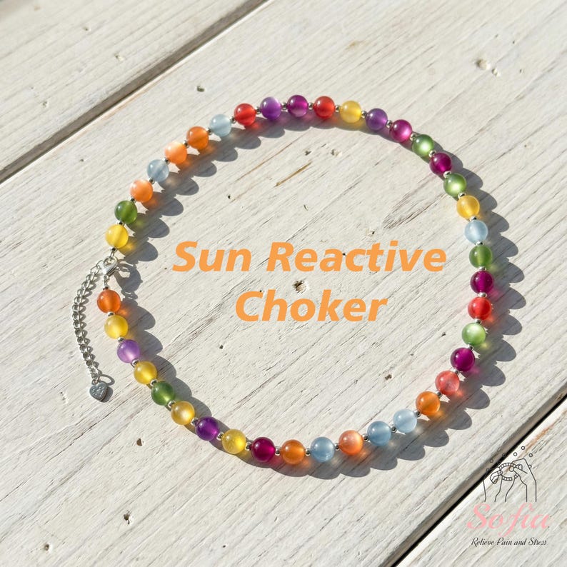 May include: A circular choker necklace featuring a continuous strand of multicolored translucent beads in shades of red, orange, yellow, green, blue, and purple. The necklace includes a silver-toned metal chain extender with a small heart charm.
