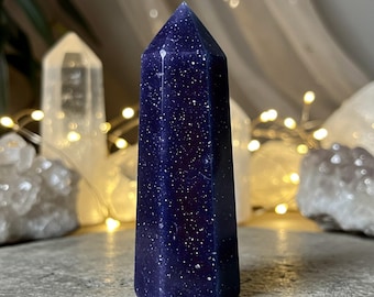 May include: A dark blue crystal point with a starry, glittery texture. The crystal is polished and has a pointed tip.