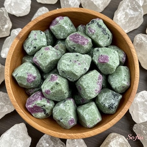 May include: A wooden bowl filled with green and pink tumbled stones. The stones have a speckled appearance and are arranged in a random pattern.
