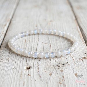 Pode incluir: Uma pulseira circular de contas composta por pequenas pedras lisas, translúcidas, de cor branca e cinzenta. Cada conta individual apresenta um brilho iridescente subtil que reflete a luz, criando um brilho suave em toda a peça de joalharia.