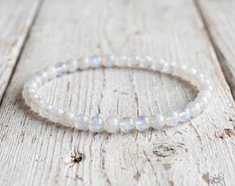 May include: A circular beaded bracelet composed of small, smooth, translucent white and grey stones. Each individual bead features a subtle iridescent sheen that reflects light, creating a soft glow across the entire strand of the jewelry piece.