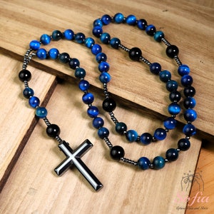 Pu&ograve; includere: Un rosario con collana di perline blu e nere con un ciondolo a croce in metallo. Le perline sono in occhio di tigre.