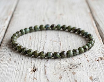 May include: A circular beaded bracelet composed of small, round, olive-green stones featuring dark brown veining throughout. The beads are uniform in size and strung together in a continuous loop, displaying natural color variations and textures.