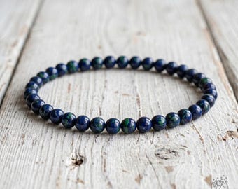 May include: A circular beaded bracelet composed of small, polished spherical stones. The beads feature a deep navy blue base color with distinct, mottled patches of vibrant forest green throughout the surface of each individual stone.