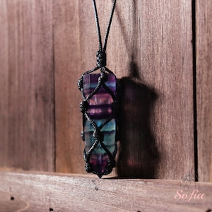 May include: A multi-colored fluorite crystal pendant wrapped in black macrame cord. The crystal is a deep purple, blue, and green color. The cord is tied in a knot at the top of the pendant.