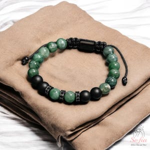 May include: A green and black beaded bracelet with a black cord closure. The bracelet features round green beads with black accents and black beads with silver accents.