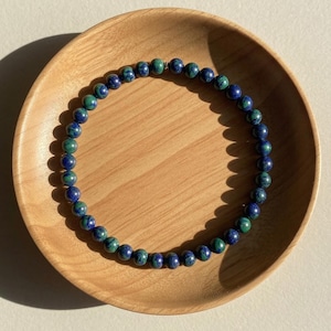 May include: A circular beaded necklace featuring polished spherical stones in deep shades of royal blue and forest green. The beads are uniform in size and strung together in a continuous loop, showcasing natural colour variations and patterns.