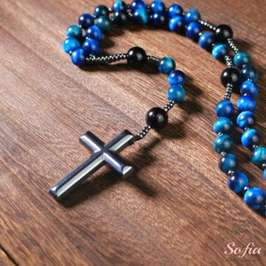 Pu&ograve; includere: Un rosario blu e nero con una croce d'argento. Le perle sono in occhio di tigre.