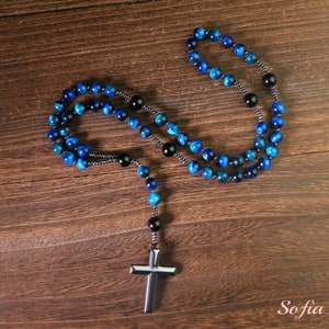 Pu&ograve; includere: Un rosario di perline blu e nere con un ciondolo a croce in metallo. Le perline sono fatte di pietra di occhio di tigre.
