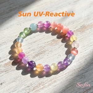 Può includere: Un braccialetto circolare composto da perline rotonde e lisce multicolori nelle tonalità viola, rosa, arancione, giallo, verde e blu. Il testo Sun UV-Reactive è stampato in arancione sopra il braccialetto e la parola Sofia è stampata sotto.