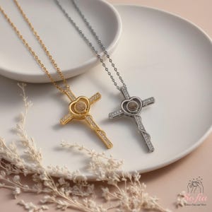 Puede incluir: Dos collares de cruz, uno dorado y otro plateado, cada uno con un centro en forma de coraz&oacute;n y una cadena delicada. Las cruces est&aacute;n adornadas con peque&ntilde;os detalles brillantes. Los collares descansan sobre un plato blanco.