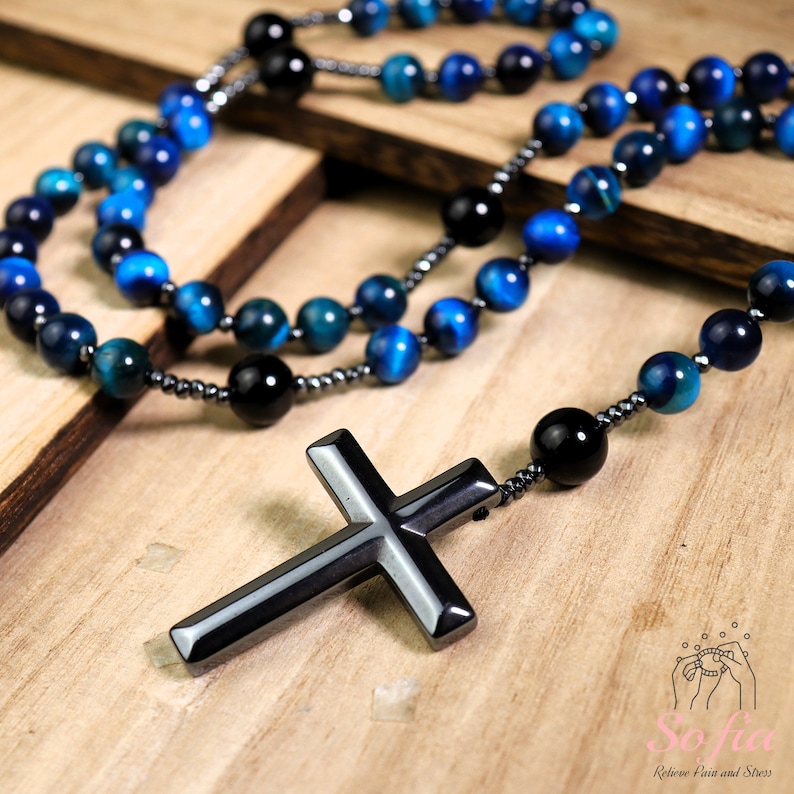 Pu&ograve; includere: Un rosario con perline blu e nere e un grande ciondolo a croce in ematite nera.