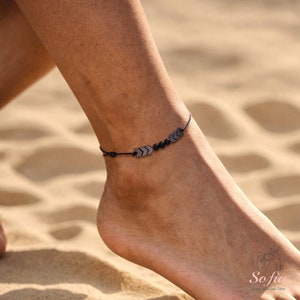 May include: A black ankle bracelet with small arrow-shaped charms and black beads.