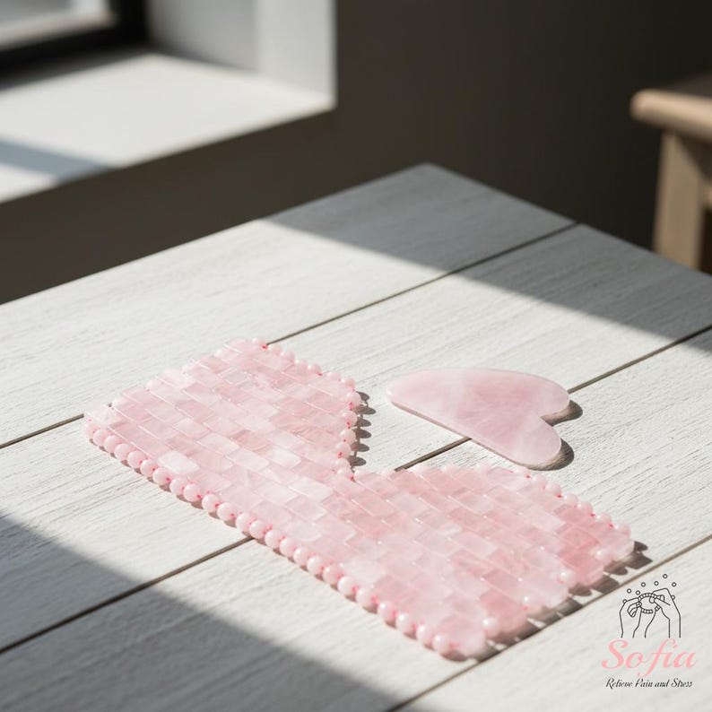 May include: Two pink rose quartz facial massage tools on a white wooden surface. One is a rectangular eye mask, and the other is a heart-shaped gua sha tool. The tools are made of small, rectangular pieces of rose quartz.
