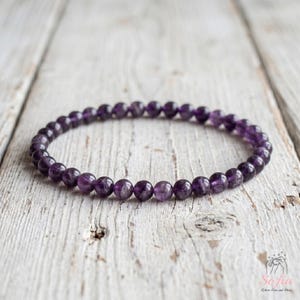 May include: A circular bracelet composed of small, smooth, spherical purple amethyst beads strung together. The beads exhibit natural variations in deep violet and translucent purple tones, forming a continuous, uniform loop of polished gemstone spheres.