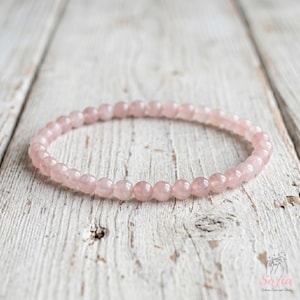May include: A circular bracelet composed of small, smooth, pale pink rose quartz beads strung together in a continuous loop. The beads are uniform in size and shape, featuring a translucent, soft pink color throughout the entire piece.
