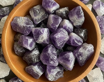 May include: A wooden bowl filled with amethyst crystals. The crystals are various shades of purple and have a rough, natural texture.