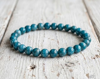 May include: A circular bracelet composed of numerous smooth, round, teal-colored gemstone beads strung together. The beads exhibit natural variations in color and texture, ranging from deep ocean blue to lighter turquoise tones throughout the piece.