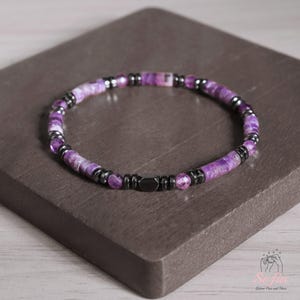 May include: A purple and black beaded bracelet with a magnetic clasp. The beads are made of amethyst and hematite.