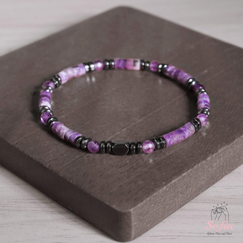 May include: A purple and black beaded bracelet with a magnetic clasp. The beads are made of amethyst and hematite.