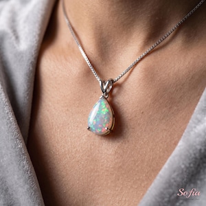 May include: A teardrop-shaped opal pendant set in a silver-toned metal prong setting, suspended from a delicate silver-toned box chain necklace. The opal displays a vibrant play-of-color with flashes of red, green, and blue against a white base.