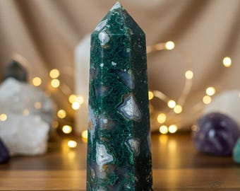 May include: A green, white, and brown agate crystal point. The crystal is polished and has a smooth, glassy surface. The point is about 6 inches tall.