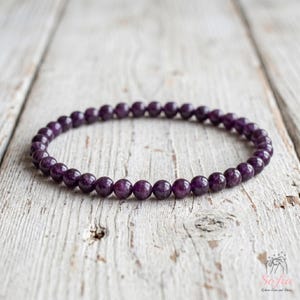May include: A circular bracelet composed of small, smooth, deep purple spherical beads. The beads are uniform in size and arranged in a continuous loop, showcasing a consistent dark violet hue throughout the entire piece of jewelry.