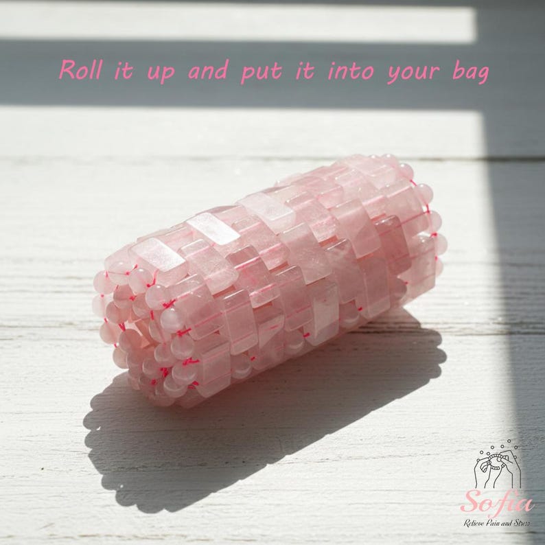 May include: A pink rose quartz beauty tool, cylindrical in shape, composed of small, rectangular stones. The text "Roll it up and put it into your bag" is written in pink. The tool is designed to relieve pain and stress.