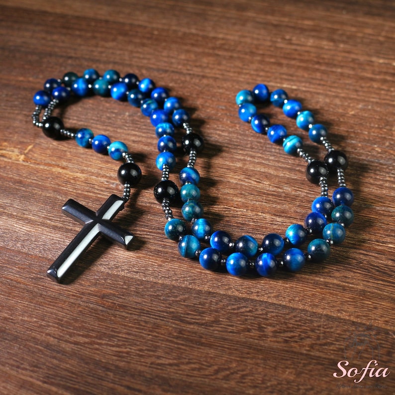 Pu&ograve; includere: Un rosario di perline blu e nere con un ciondolo a croce nera. Le perline sono fatte di pietra di occhio di tigre.