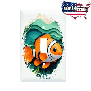 May include: A light switch cover featuring a colorful cartoon clownfish swimming in a green and blue ocean scene. The fish has orange and white stripes and a black eye.