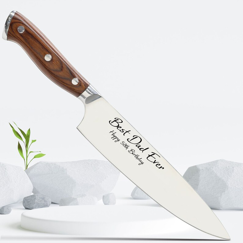 Puede incluir: Un cuchillo de chef de acero inoxidable con mango de madera. La hoja est&aacute; grabada con el texto "Best Dad Ever" y "Happy 50th Birthday".