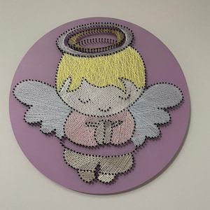 Può includere: Un'opera d'arte con fili raffigurante un angelo. L'angelo ha un'aureola gialla, capelli gialli e ali azzurre. Il corpo dell'angelo è rosa e beige, su uno sfondo lilla.