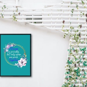 Puede incluir: Un estampado enmarcado en color turquesa con el texto "Change is possible, but only when we work Together." El texto está rodeado por un círculo dorado y detalles florales en morado y blanco. El marco es negro.