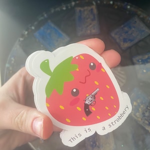 May include: A red and green cartoon strawberry with a small gun in its hand. The text "This is a strobbery" is written below the strawberry.